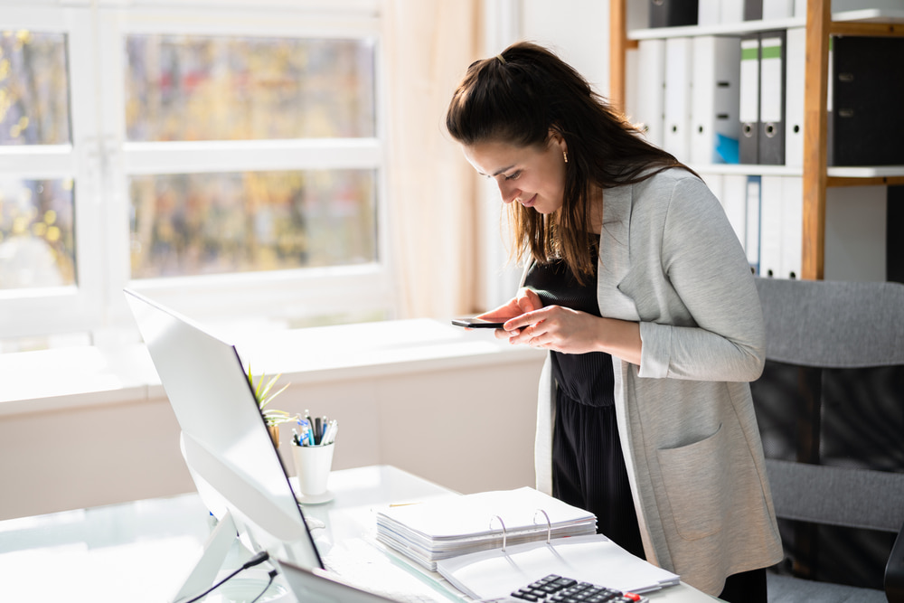 Real estate agent happily using her smartphone for mobile document capture, showcasing the ease of automated document processing.
