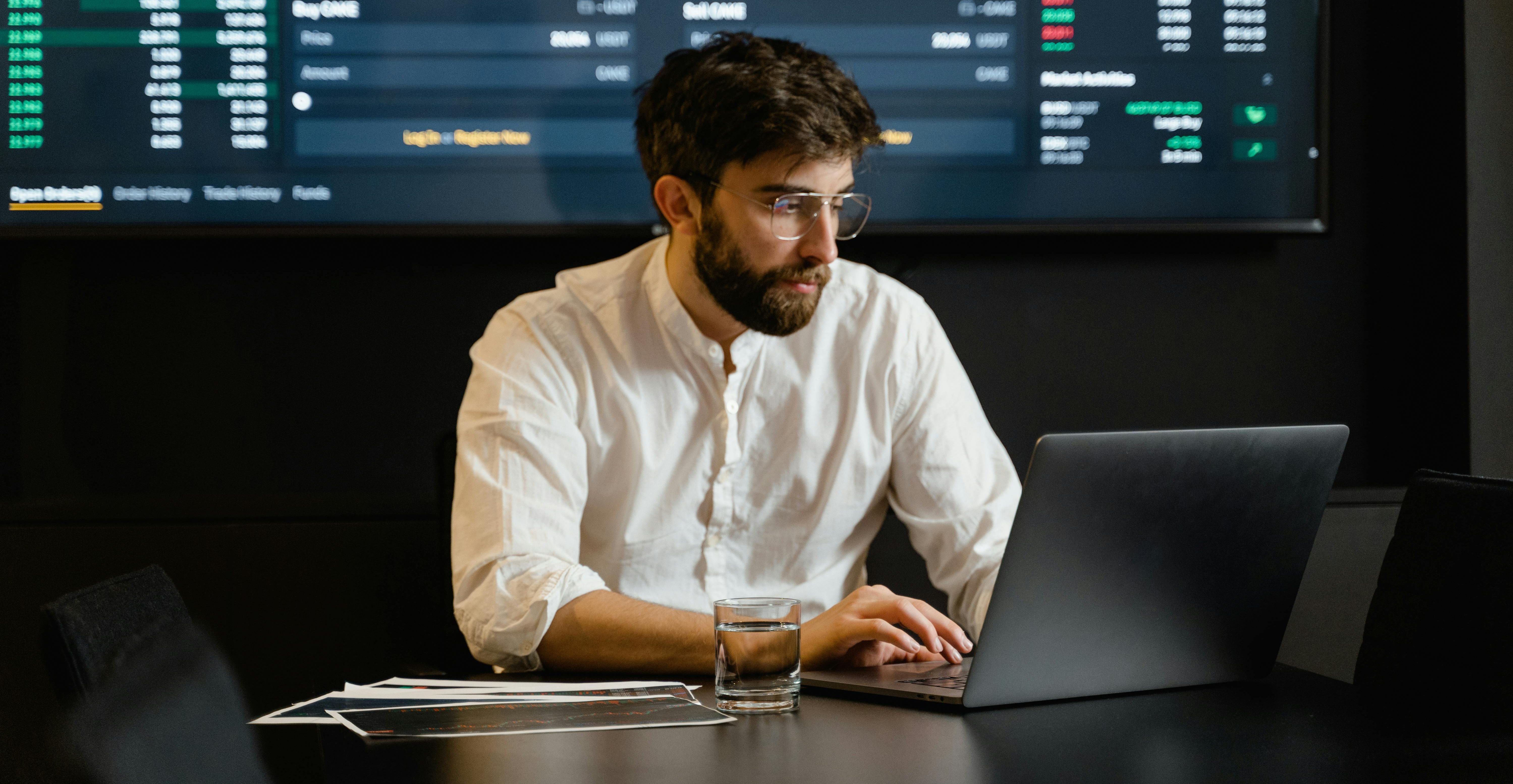Financial analyst working on a laptop, performing financial data extraction and analysis with AI tools, stock market data visible in the background.
