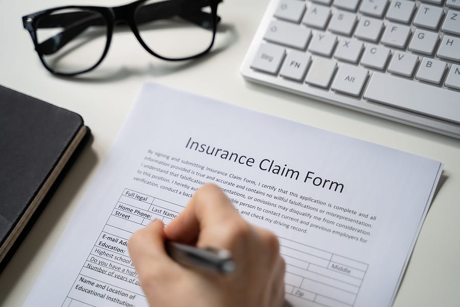 Person filling out an Insurance Claim Form by hand, illustrating the traditional claims process before AI automation and claims processing.